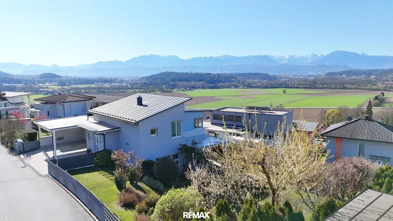Moderne Villa mit Carport und weitem Blick über grüne Felder und die umliegende Berglandschaft.