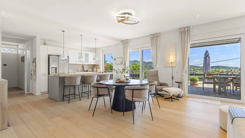Helles, offenes Wohn-Esszimmer mit moderner Küche, Holzboden und Zugang zu einer großen Terrasse mit Weitblick.