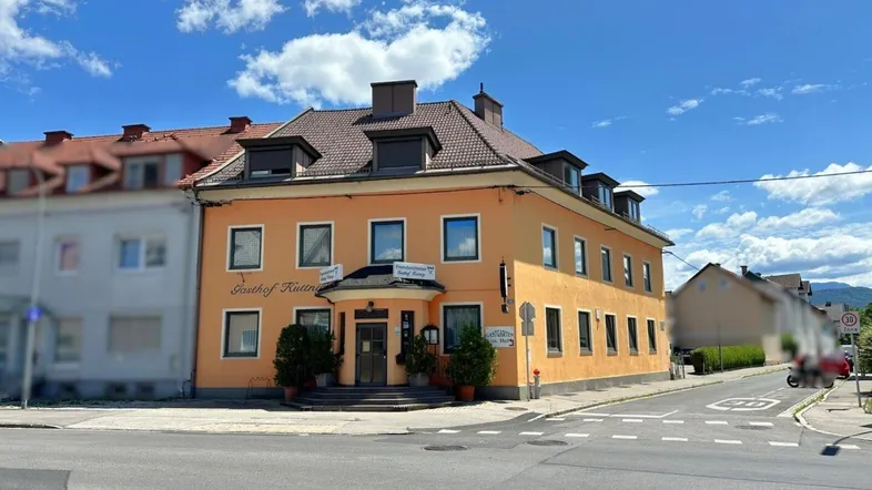 Gebäudeansicht eines Gasthofs an einer Straßenecke mit orangefarbener Fassade und mehreren Fenstern.