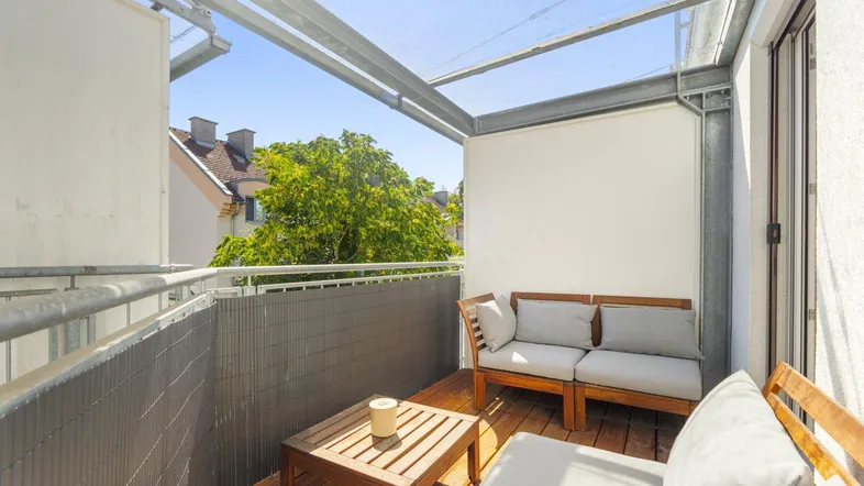 Heller Balkon mit Holzboden, bequemen Gartenmöbeln und schützender Überdachung für entspannte Stunden im Freien.