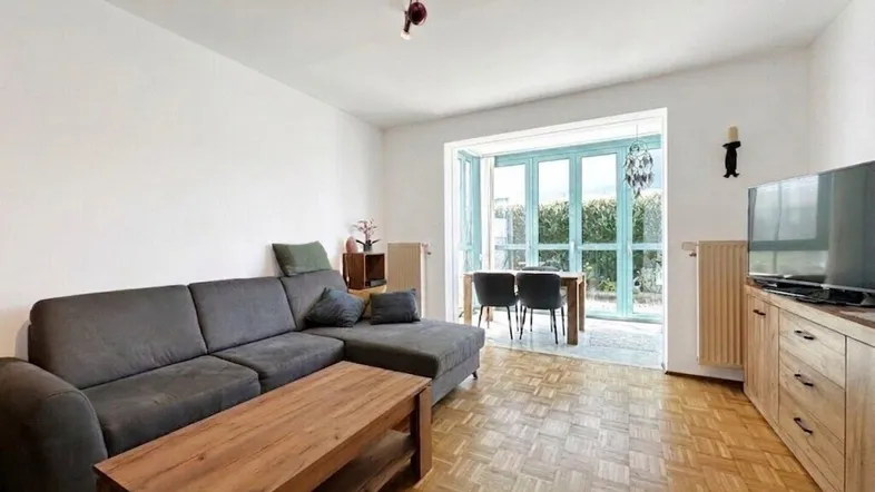 Helles Wohn- und Esszimmer mit Parkettboden, bequemer Couch und Zugang zum Außenbereich.