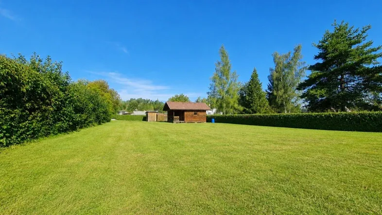 Weitläufiger grüner Garten mit einem kleinen Holzschuppen unter blauem Himmel.