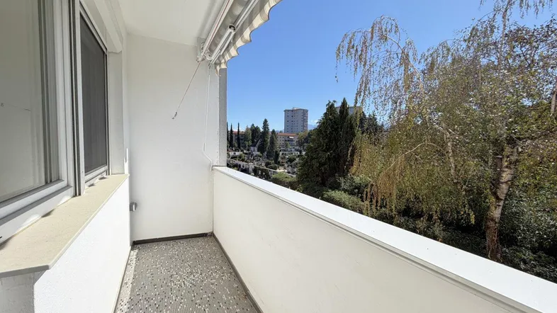 Geräumiger Balkon mit Markise und weitem Blick über grüne Bäume und die Stadt.