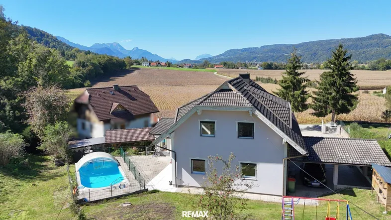 Luftaufnahme des Hauses mit Pool, Spielplatz und weitem Blick auf die umliegende Landschaft und Berge.