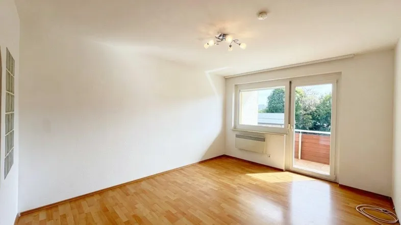Helles Zimmer mit Parkettboden und Zugang zu einem Balkon, ideal als Wohn- oder Schlafbereich.