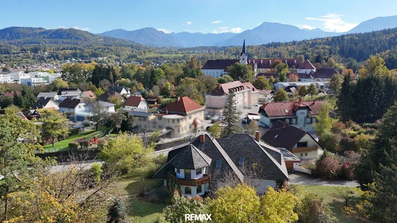 Luftaufnahme eines Wohngebiets mit Häusern, Bergen im Hintergrund und viel Grün.