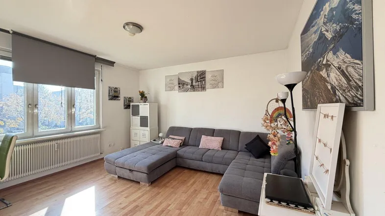 Helles Wohnzimmer mit großem Ecksofa, Holzfußboden und Blick nach draußen durch die Fenster.