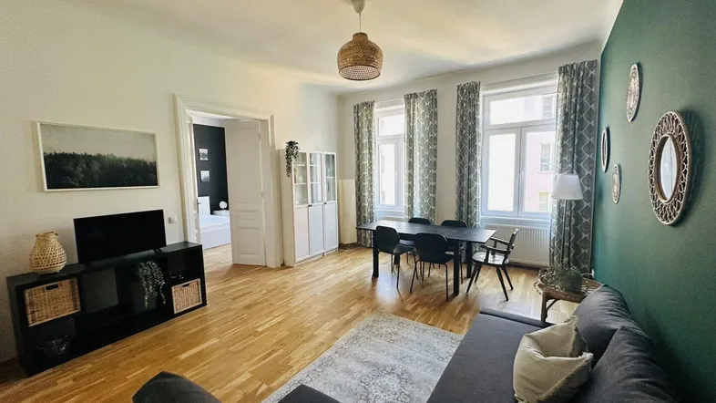 Helles Wohn- und Esszimmer mit Parkettboden, grüner Akzentwand und großzügigen Fenstern.