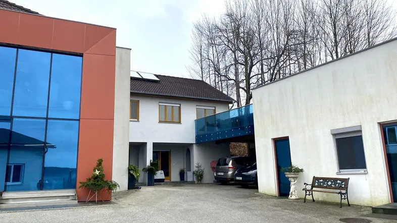 Moderner Gebäudekomplex mit blauer Glasfassade und überdachtem Parkbereich, umgeben von Bäumen.