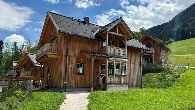 Traditionelles Holzhaus im alpinen Stil mit Satteldach und Balkonen, umgeben von grünen Wiesen und Bergen.