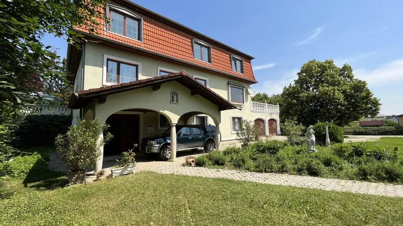 Geräumiges Haus mit Carport und großem Gartenbereich unter blauem Himmel.