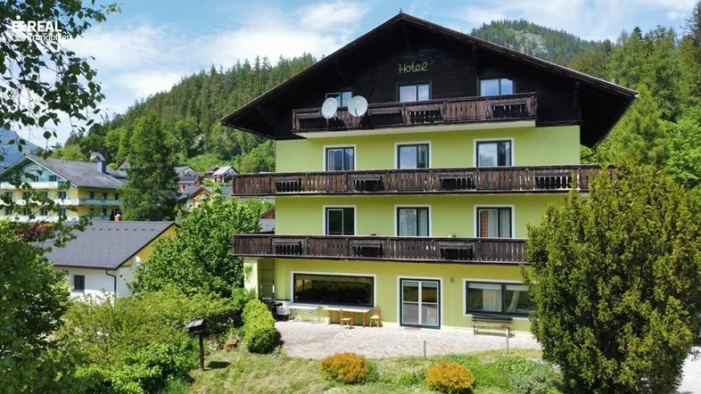 Traditionelles Gebäude mit grüner Fassade, Holzbalkonen und Blick auf die umliegende Berglandschaft.
