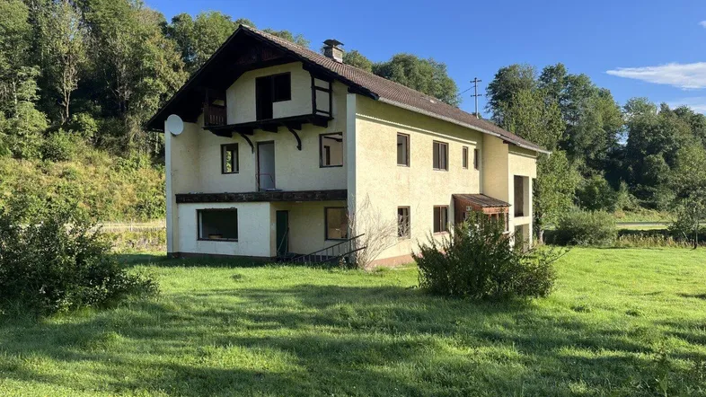 Ländliches Haus mit einfacher Fassade und großem Grundstück in grüner Umgebung.