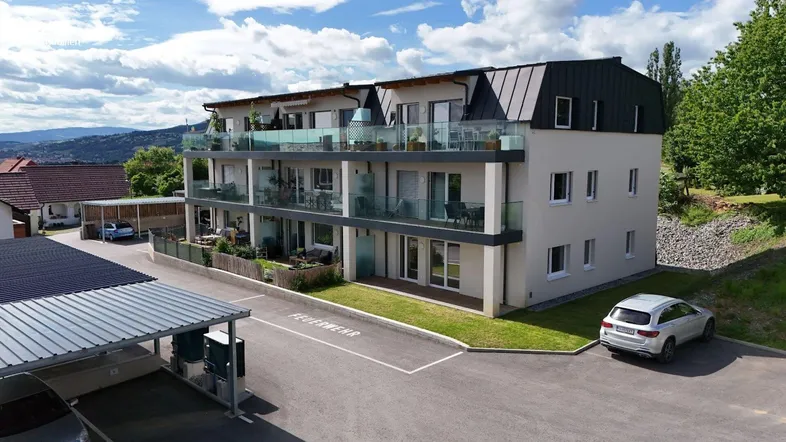 Modernes Mehrfamilienhaus mit mehreren Balkonen und Carports in grüner Umgebung.