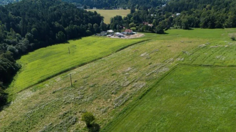 Weitläufige Luftaufnahme der grünen Landschaft mit Feldern, Wäldern und einem historischen Gebäude in der Ferne.