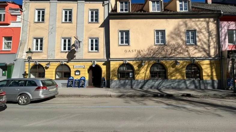 Historisches Gebäude mit gelber Fassade und traditioneller Architektur an einer belebten Straße mit parkenden Autos.