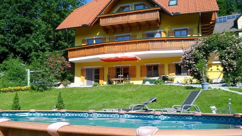 Gelbes Haus mit rotem Ziegeldach, mehreren Balkonen, einem gepflegten Garten und einem oberirdischen Pool.