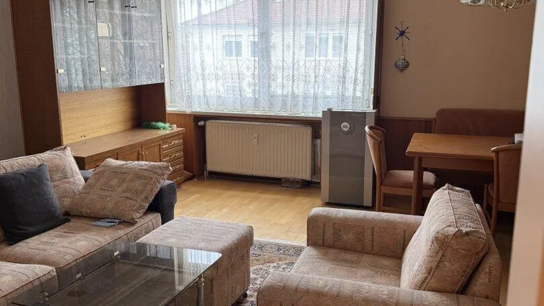 Wohnbereich mit Sofa, Couchtisch und Blick auf das Fenster mit Vorhängen.
