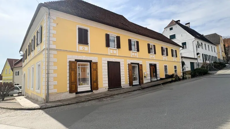 Gelbe Fassade eines historischen Gebäudes mit traditionellen Fensterläden und dekorativen Elementen.