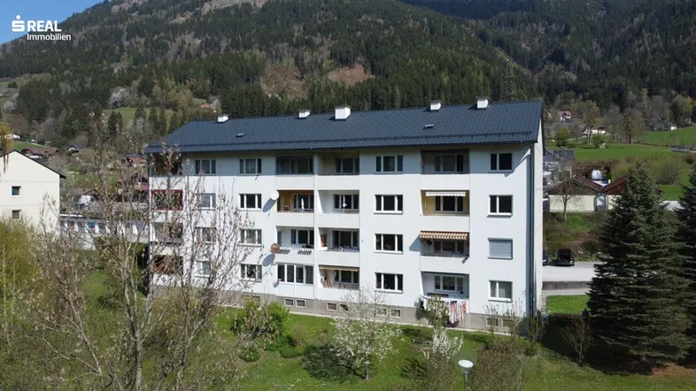 Mehrfamilienhaus in ländlicher Umgebung mit weißer Fassade und Blick auf die Berge.