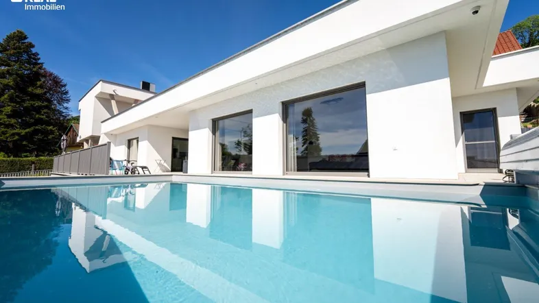 Moderne Villa mit großem Außenpool und weißer Fassade unter blauem Himmel.