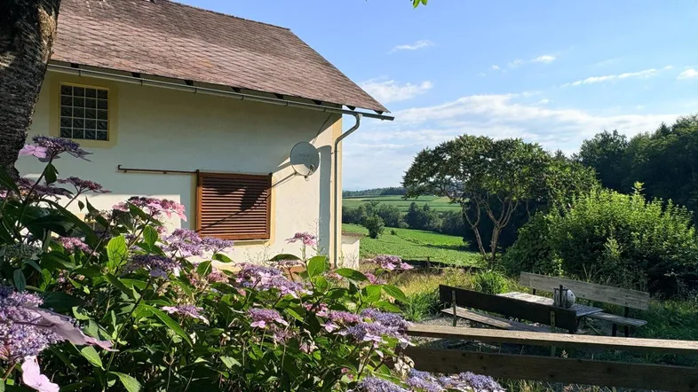Hausfassade mit blühenden Hortensien und weitem Blick über die grüne Landschaft.