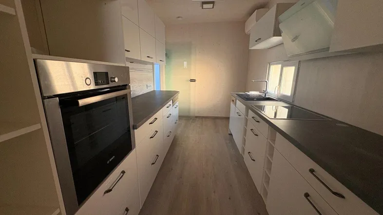 Moderne Küche mit weißen Schränken, dunkler Arbeitsplatte und integriertem Backofen von Bosch.