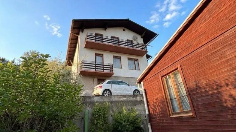 Mehrstöckiges Wohnhaus mit Balkonen und angrenzendem Nebengebäude in ländlicher Umgebung.