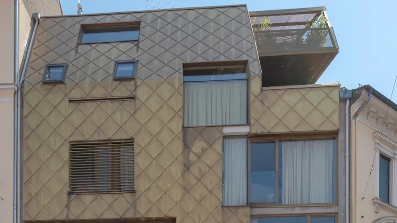 Moderne Fassade mit rautenförmigen Metallplatten und verschiedenen Fenstern.