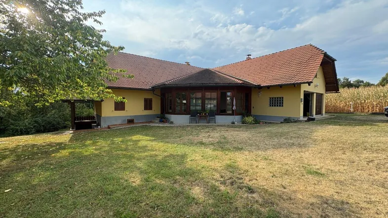 Haus mit gelber Fassade, rotem Ziegeldach und großem Gartenbereich unter blauem Himmel.
