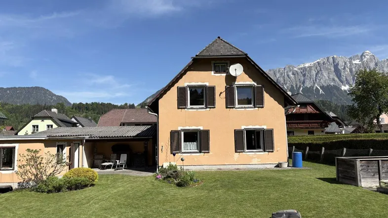 Traditionelles Haus mit Garten und Bergblick unter strahlend blauem Himmel.