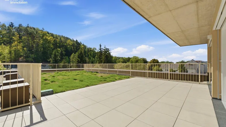 Große geflieste Terrasse mit Rasenfläche und weitem Blick ins Grüne.