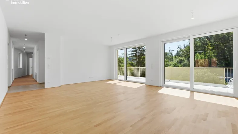 Helles, leeres Wohnzimmer mit Parkettboden und Zugang zu einem großen Balkon.