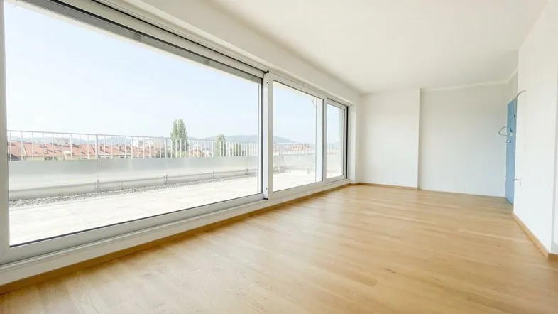 Helles, leeres Zimmer mit großen Schiebefenstern und Zugang zu einer Terrasse mit Stadtblick.