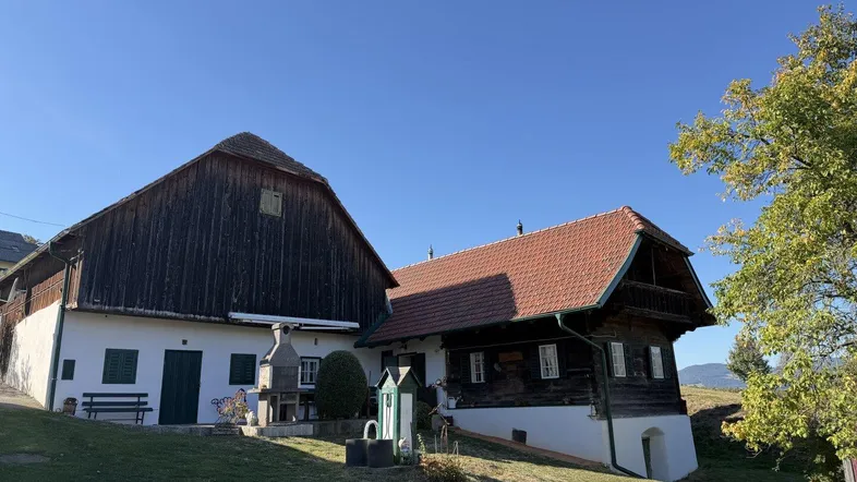 Traditionelles Bauernhaus mit Holzbalkonen und Ziegeldach in ländlicher Umgebung unter blauem Himmel.