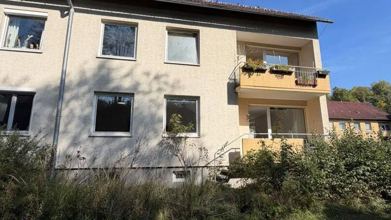Mehrfamilienhaus mit Balkonen und begrüntem Vorgarten unter blauem Himmel.