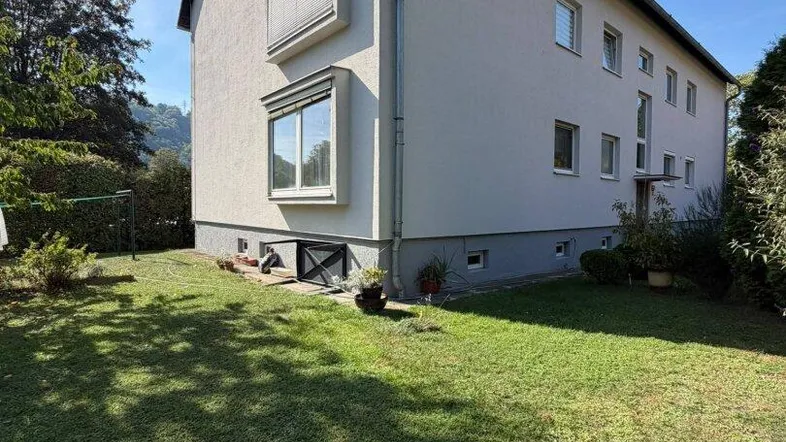 Seitenansicht des Mehrfamilienhauses mit gepflegtem Rasen und Blick auf die umliegende grüne Landschaft.