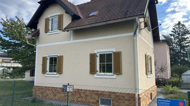 Seitenansicht des Hauses mit Fensterläden, Satteldach und einem kleinen Vorgarten.