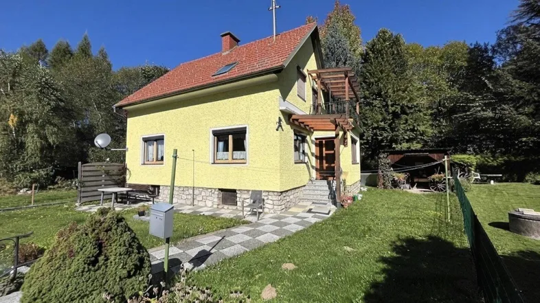 Gelbes Einfamilienhaus mit rotem Ziegeldach und gepflegtem Vorgarten unter blauem Himmel.