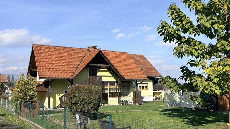 Großzügiger Gartenbereich mit Rasenfläche und Sitzgelegenheiten vor dem Haus unter blauem Himmel.