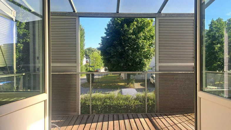 Helle, überdachte Loggia mit Holzboden und weitem Blick ins Grüne und auf die Straße.