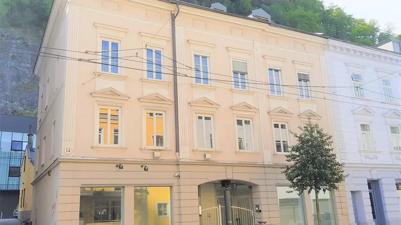 Historisches Gebäude mit heller Fassade und großen Fenstern an einer Straße gelegen.