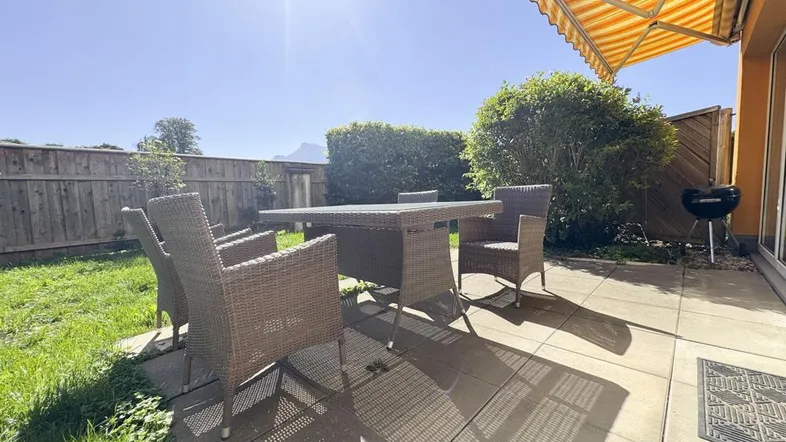 Sonnige Terrasse mit Gartenmöbeln, Rasenfläche und Markise, ideal für entspannte Stunden im Freien.