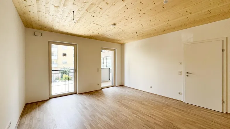 Helles, leeres Zimmer mit Holzbalkendecke und Zugang zu zwei französischen Balkonen.