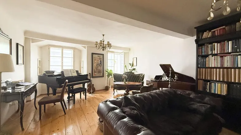 Geräumiges Wohnzimmer mit Holzdielenboden, Flügel, Bücherregal und klassischer Einrichtung.