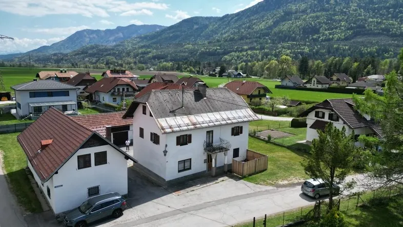 Luftaufnahme eines Wohnhauses mit Satteldach und umliegender ländlicher Landschaft vor einer Bergkulisse.