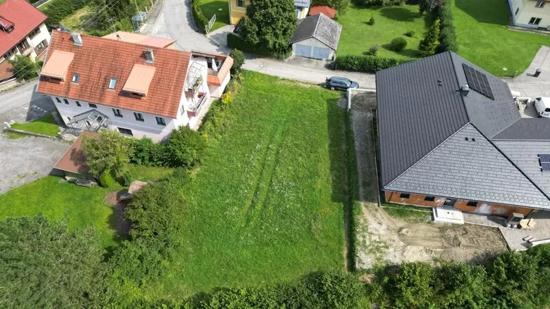 Luftaufnahme eines grünen Grundstücks zwischen zwei Wohnhäusern in ländlicher Umgebung.