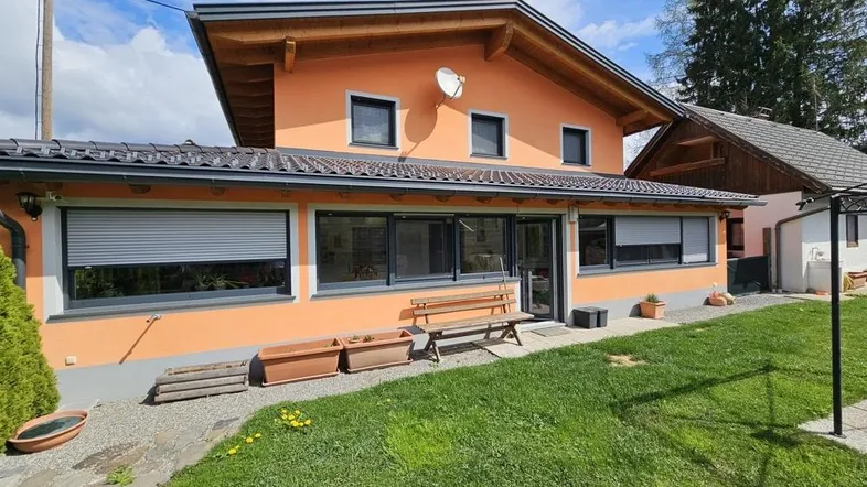 Vorderansicht des Hauses mit orangefarbener Fassade, großen Fenstern und gepflegtem Vorgarten.