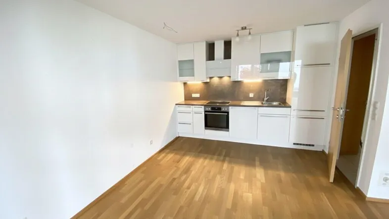 Moderne, offene Küche mit weißen Hochglanzfronten und Holzboden in einem hellen Raum.