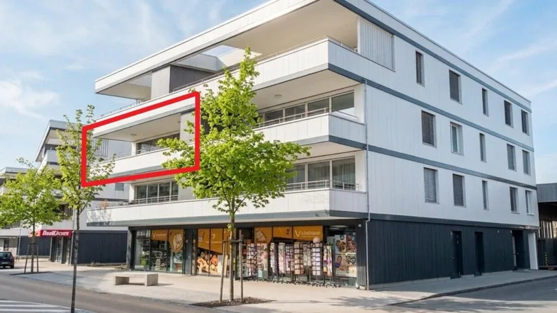 Modernes Mehrfamilienhaus mit Geschäften im Erdgeschoss und Balkonen in einer städtischen Umgebung.